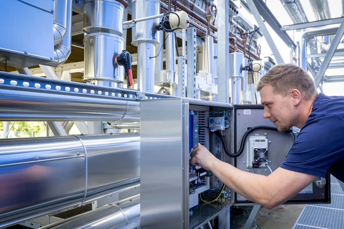 Monteur arbeitet an einem Schaltkasten unter einer Rohrleitungsbühne